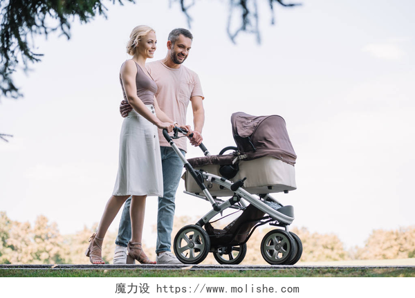 恩爱的夫妻推着婴儿车在散步快乐的父母走在公园里的婴儿马车周末